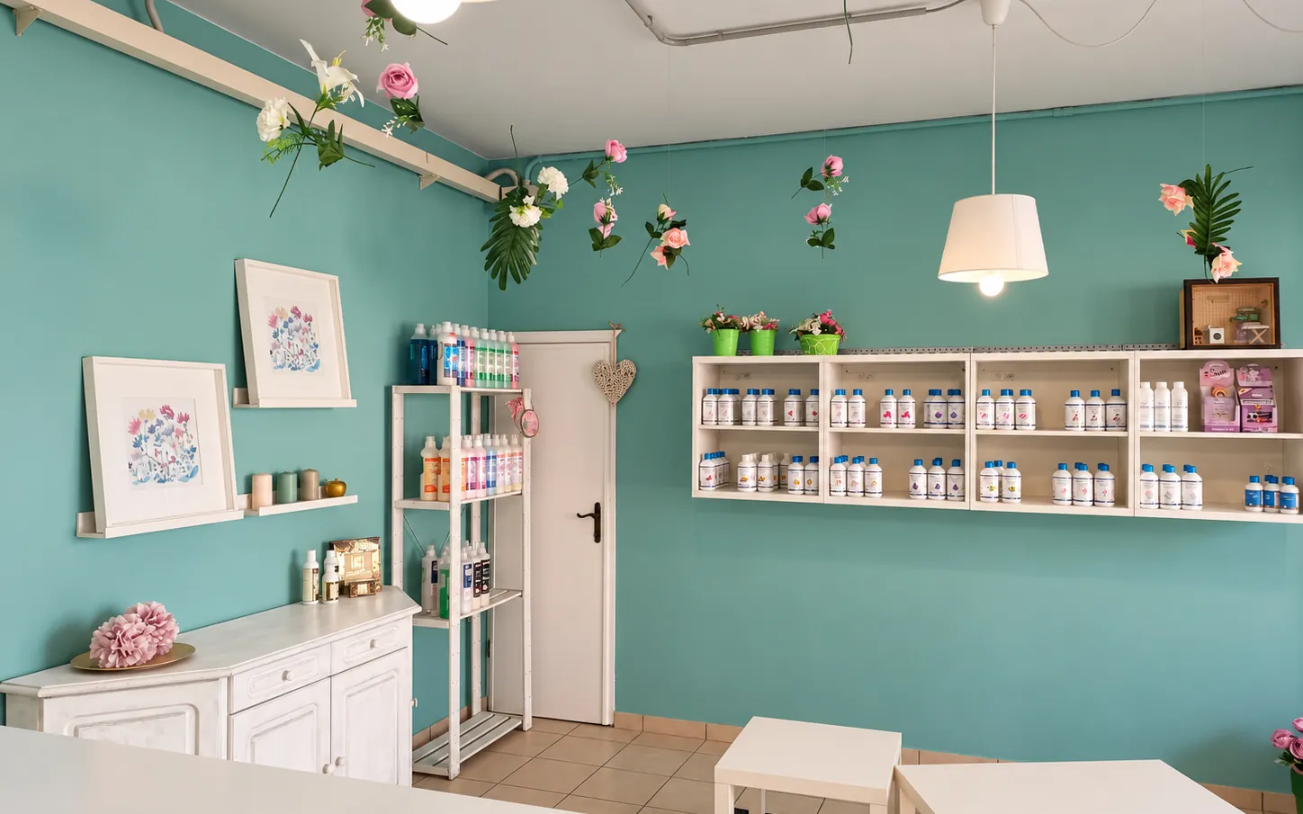 La sala vista dal bancone, con il mobile bianco, i quadri floreali e gli scaffali dei prodotti